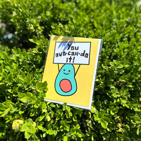 Cartoon avocado with a sign reading "you avo-can-do-it" on a green bush