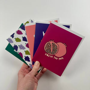 Hand holding a bundle of fruit themed cards surrounded by a white background.