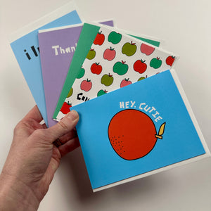 Hand holding a blue card with an orange design, surrounded by other colorful cards on a light background