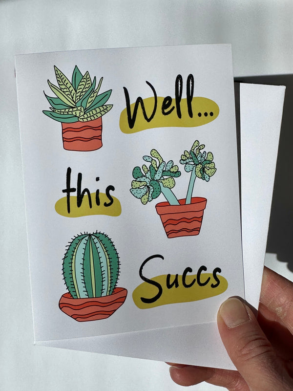 Hand holding a card with cactus and succulent illustrations and text that reads "well this succs" 